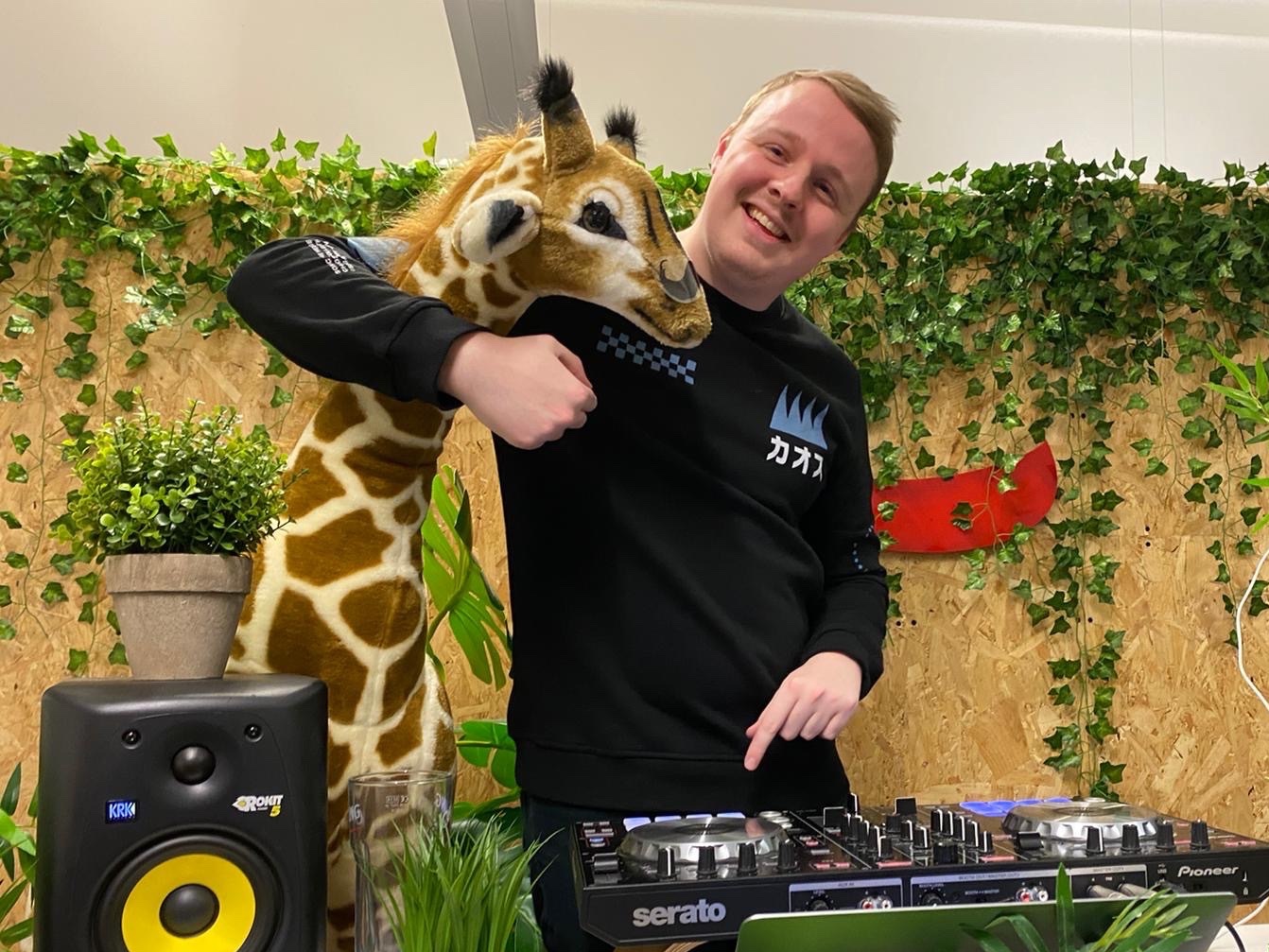 Man stood next to toy giraffe and dj decks